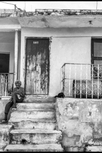 Cuban woman knitting in front of her house with her cat sleeping next to her